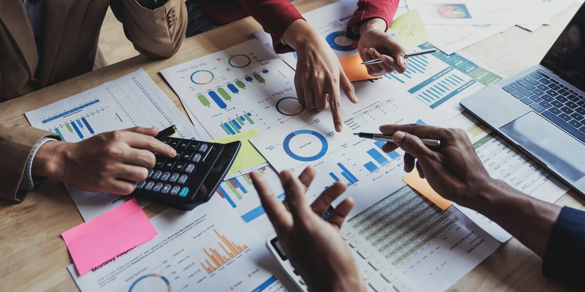 Team reviewing financial reports, charts and spreadsheets on a desk with a calculator and laptop during a business meeting.